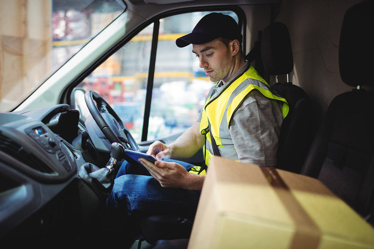 delivery drive with a parcel on the front seat of his van, checking his delivery app