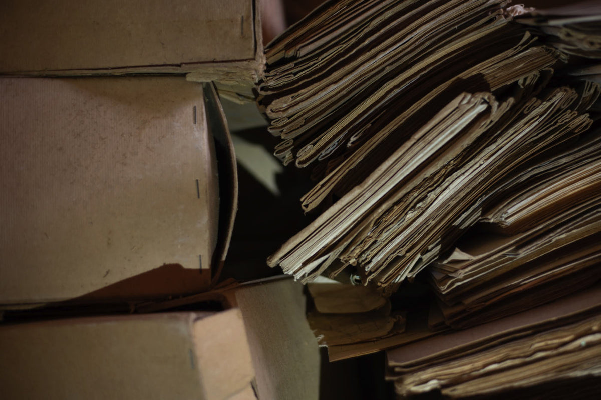 Very old and weathered cardboard boxes, stacked next to old manuscripts, news papers. 