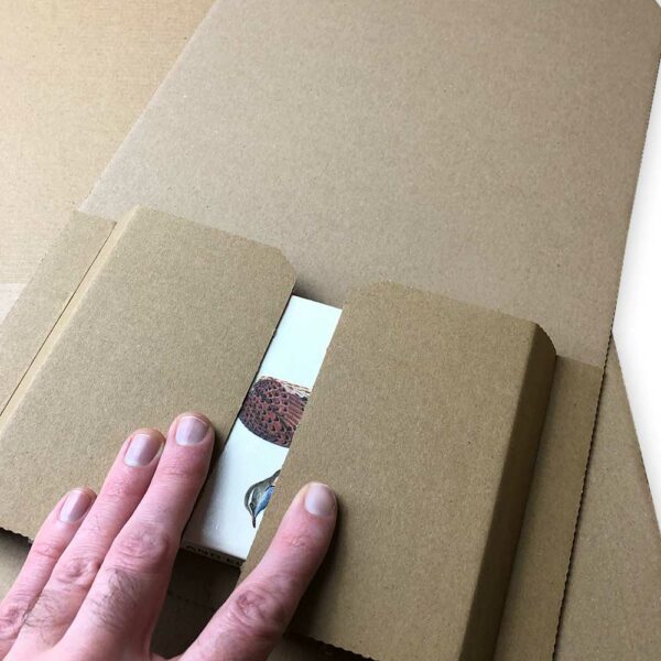 Hand holding postal wraps. Postal wraps are a highly versatile type of corrugated packaging, they have variable height which means they can be used to ship a variety of different types of order, and the item is well supported during shipment to minimise damage.
